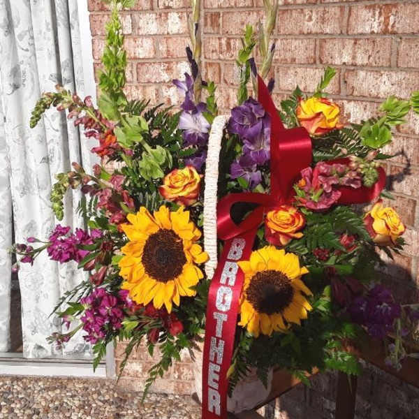 Standing floral spray with sunflowers, roses, and purple blooms on a ribboned easel