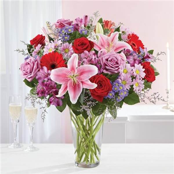 Mixed bouquet of roses, lilies, and daisies in a clear glass vase