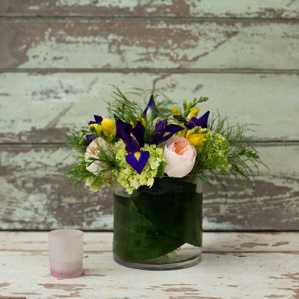 Bouquet of purple irises, yellow blooms, and pale pink roses in a glass vase
