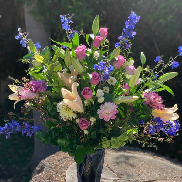 Mixed bouquet with pink roses, lilies, and blue flowers in a blue vase