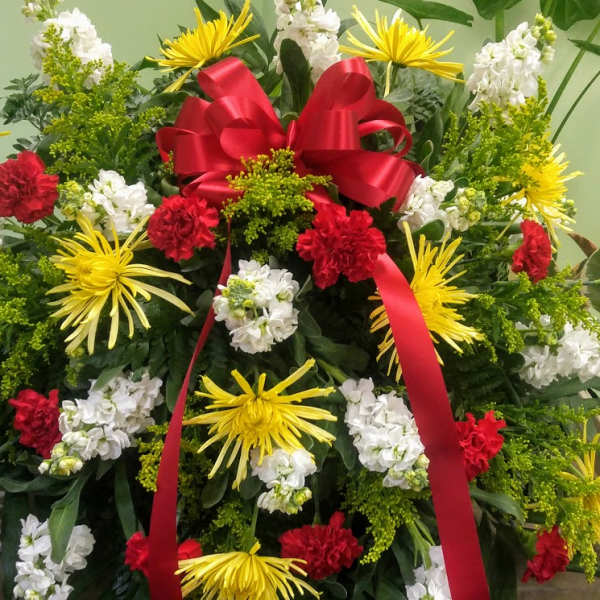 Large standing floral spray with red ribbon and yellow, white, and red flowers