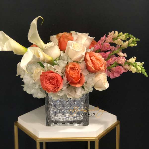 Bouquet of white calla lilies, coral roses, and pink snapdragons in a glass vase