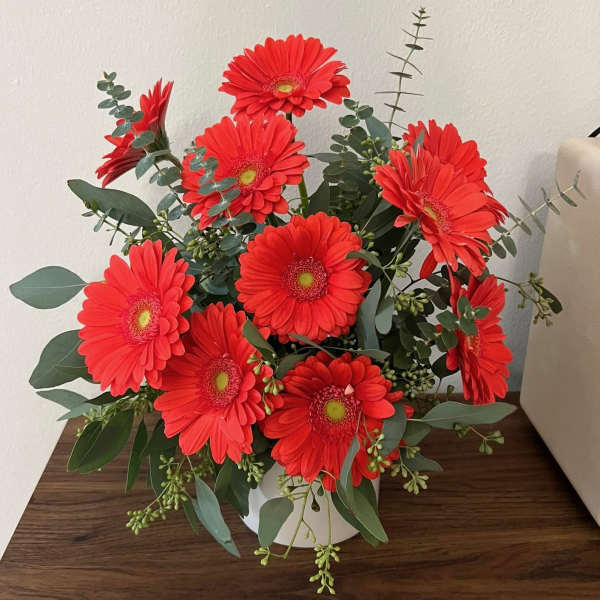 Red gerbera daisies arranged in a white vase with eucalyptus