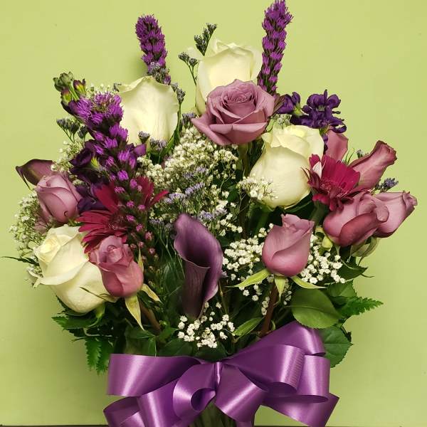 Mixed bouquet of roses, calla lilies, and purple flowers in a glass vase with a ribbon