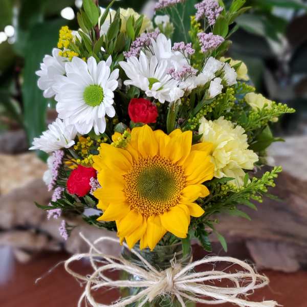 Bouquet with a sunflower, white daisies, and red carnations in a glass vase