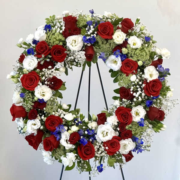 Heart-shaped wreath of red, white, and blue flowers on a black stand