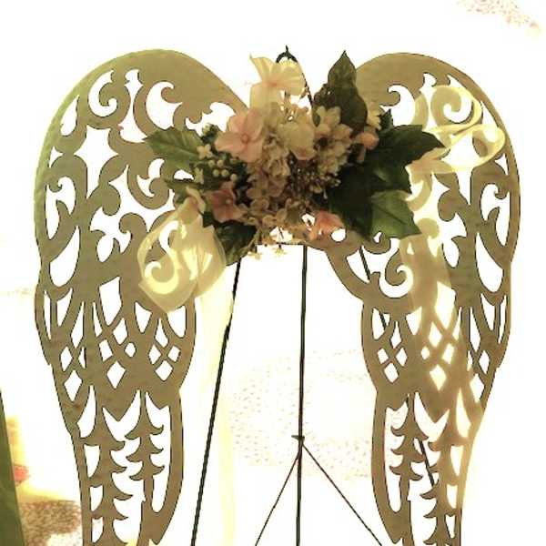 Floral arrangement on decorative angel wings with pale flowers and dark green leaves