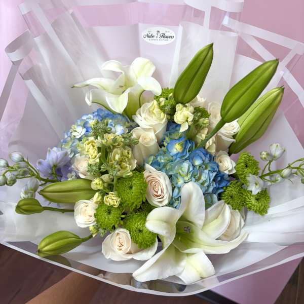 Bouquet of white lilies, blue hydrangeas, and cream roses wrapped in clear paper