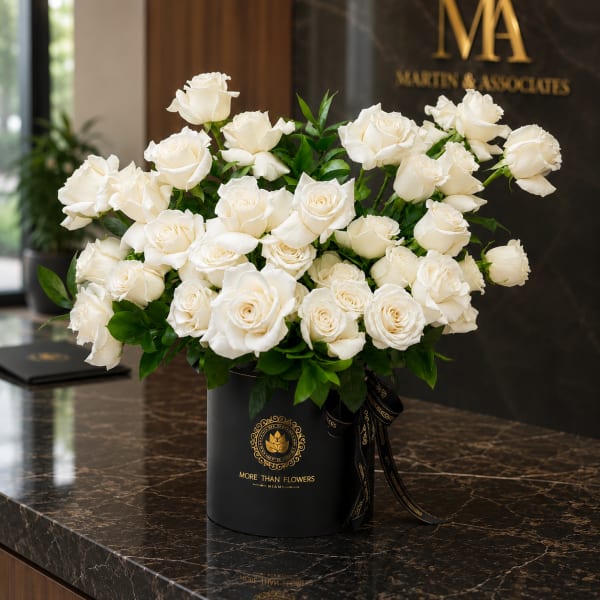 White roses arranged in a black hatbox with a ribbon