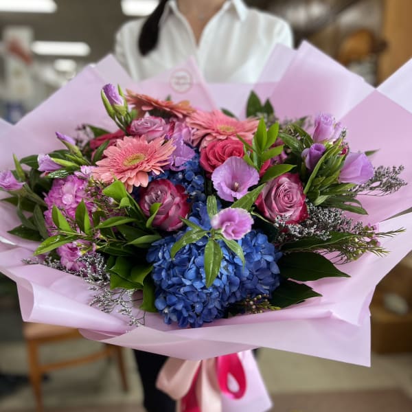Bouquet of pink and purple flowers with blue hydrangeas wrapped in pink paper