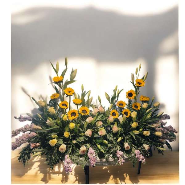 Large floral arrangement with yellow sunflowers and pale roses in a low container