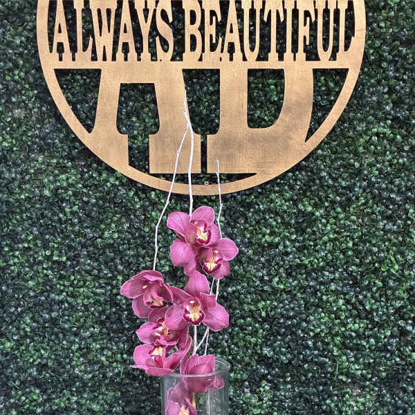 Pink orchids in a clear glass vase against a green backdrop