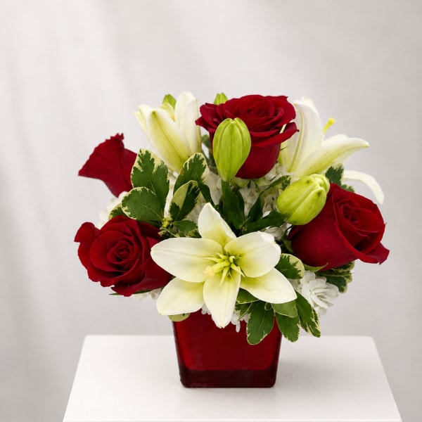 Red roses and white lilies arranged in a red square vase