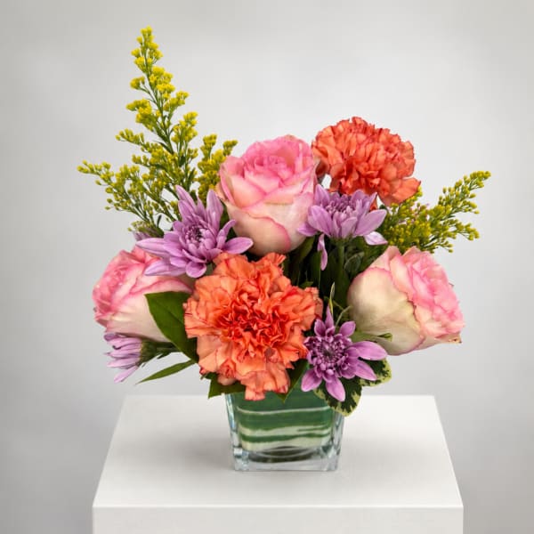 Pink roses, orange carnations, and purple daisies in a glass vase