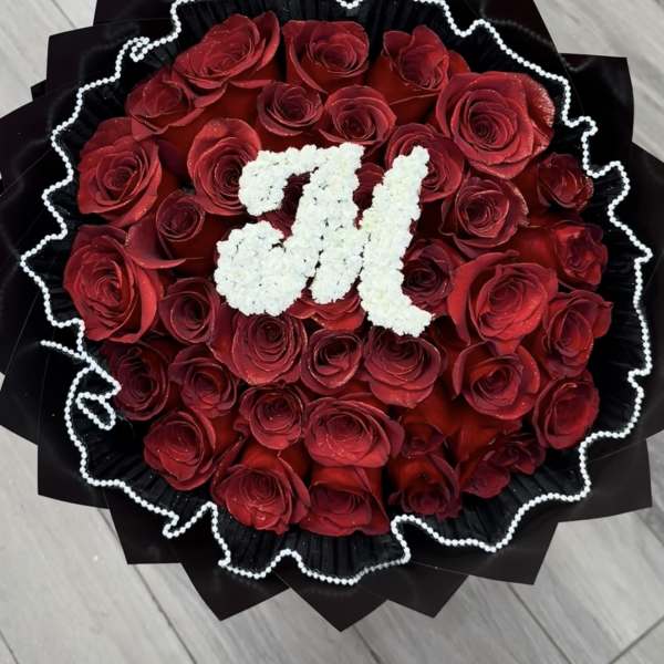 Round bouquet of red roses with a white floral monogram on black wrap