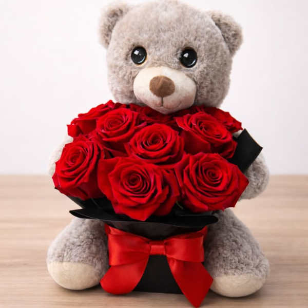 Gray teddy bear holding a bouquet of red roses with a red ribbon