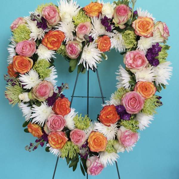 Heart-shaped floral wreath with pink and orange roses on a stand