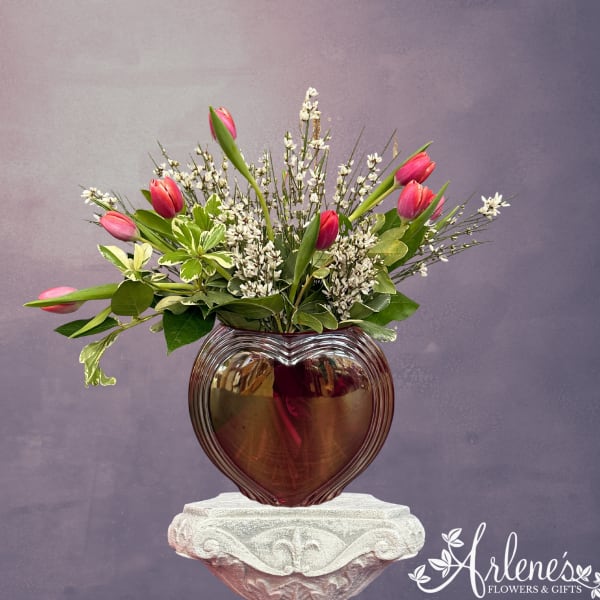 Pink tulips arranged in a heart-shaped glass vase with white filler flowers