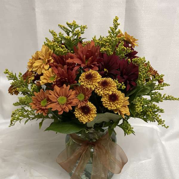 Autumn bouquet of orange, yellow, and burgundy flowers in a glass vase