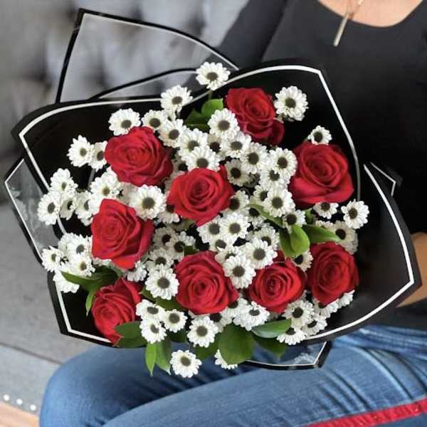 Bouquet of red roses and small white daisies wrapped in black paper