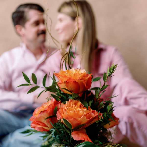 Orange roses arranged in a glass vase with greenery.