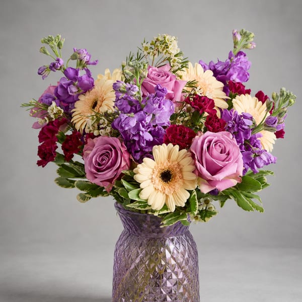 Purple and pink bouquet with cream daisies in a textured glass vase