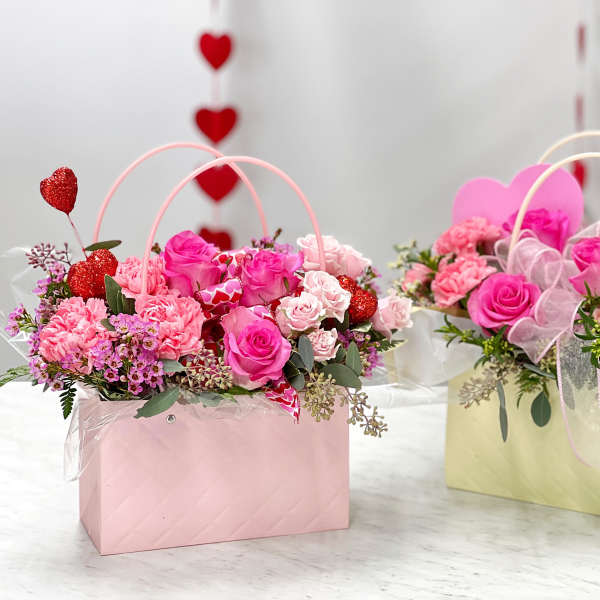 Two pink floral gift baskets with roses and carnations, decorated with heart picks