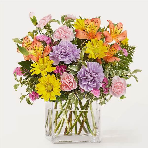 Mixed bouquet of pink, yellow, orange, and lavender flowers in a clear glass vase