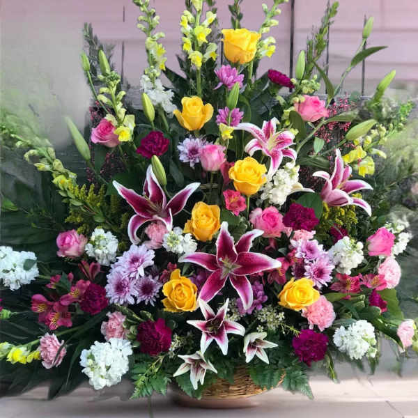 Large mixed floral arrangement with yellow roses, pink lilies, and white blooms in a basket