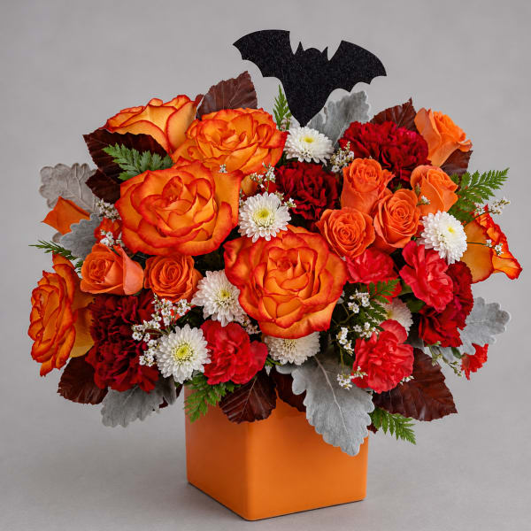 Orange and red rose arrangement in an orange vase with a bat pick