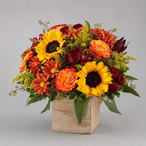 Autumn bouquet with sunflowers, orange roses, and mums in a wooden cube vase