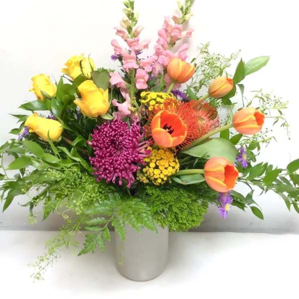 Mixed bouquet of yellow roses, orange tulips, and purple blooms in a vase