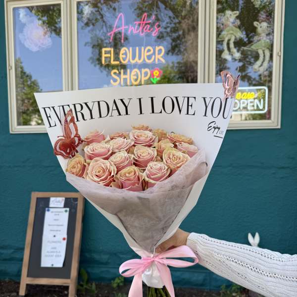 Bouquet of pink and peach roses wrapped in white paper with a pink ribbon