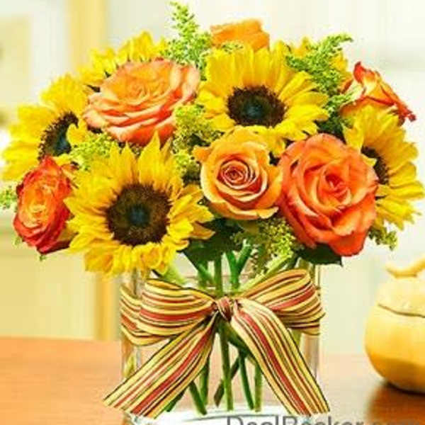 Sunflowers and orange roses in a glass vase with a striped ribbon