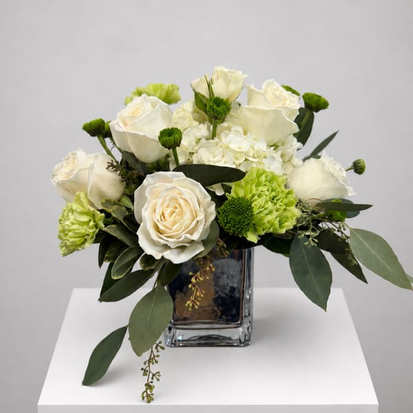 White roses and green carnations arranged in a clear square vase
