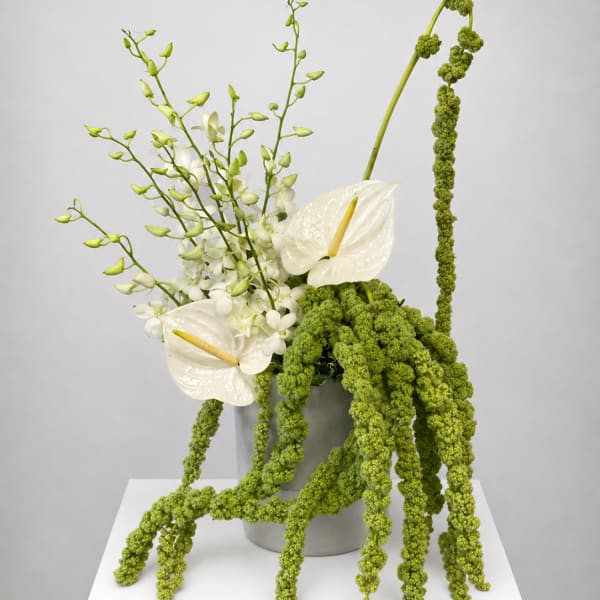 White anthuriums and orchids in a gray vase with cascading green blooms