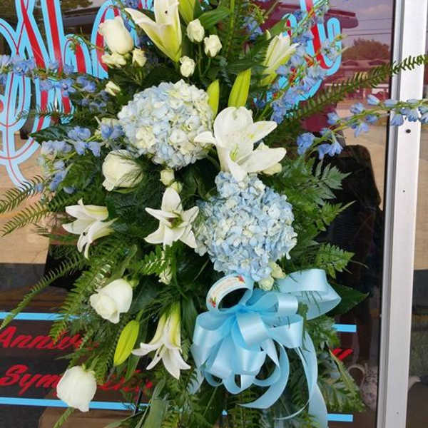 Standing floral spray with white lilies, blue hydrangeas, and a blue ribbon