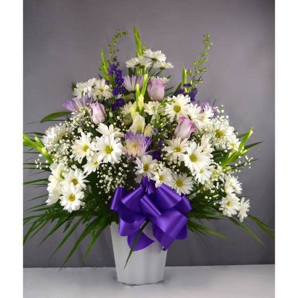 White daisies and purple flowers in a white vase with a purple ribbon
