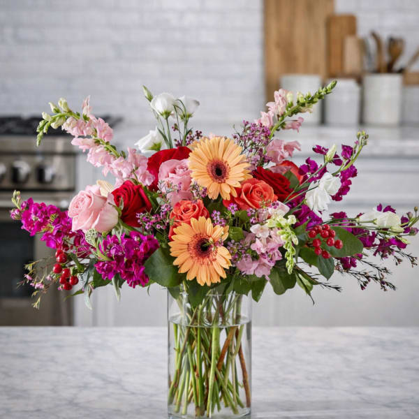 Mixed bouquet of roses, gerbera daisies, and pink blooms in a clear glass vase