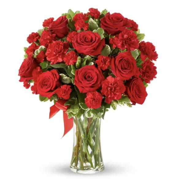 Red roses and carnations in a clear glass vase with a red ribbon