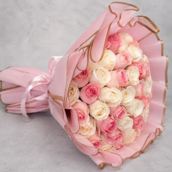 Bouquet of pink and white roses wrapped in pink paper with ribbon