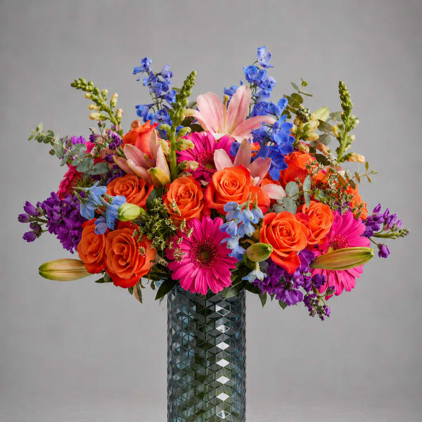 Bright mixed bouquet in a textured glass vase with roses, lilies, and daisies