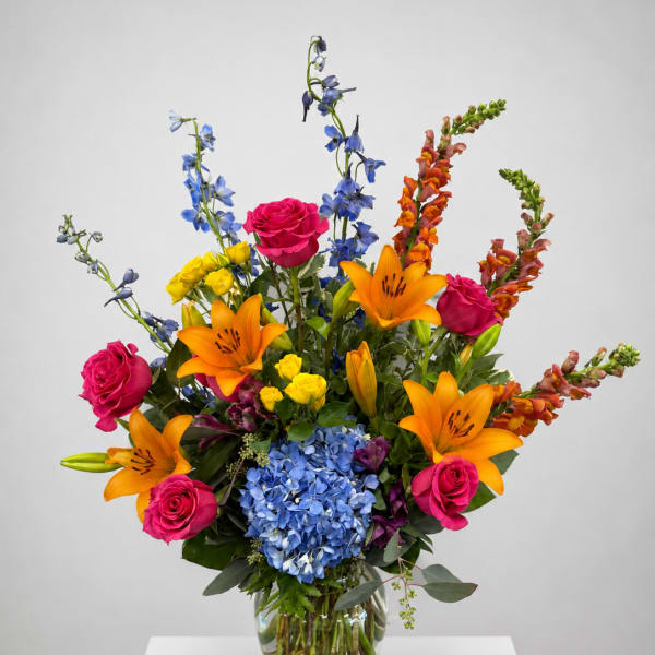 Bright mixed bouquet with roses, lilies, hydrangea, and blue delphinium in a glass vase