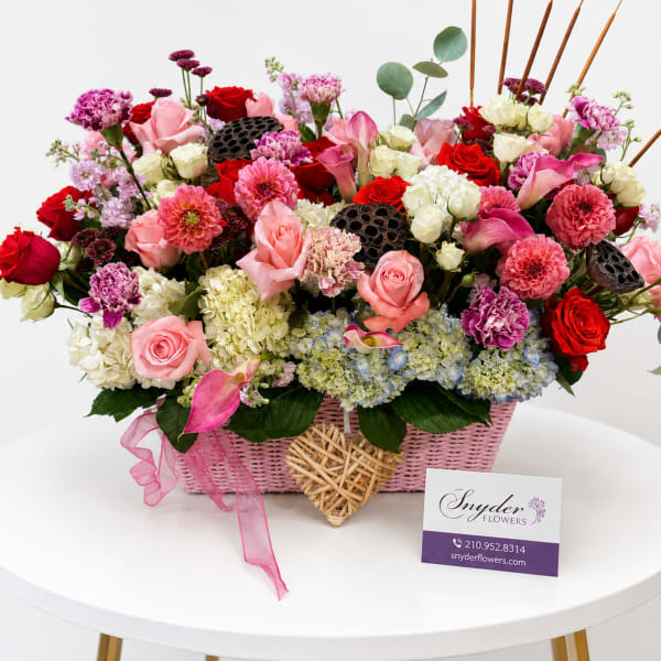 Pink and red mixed flower arrangement in a pink basket with ribbon