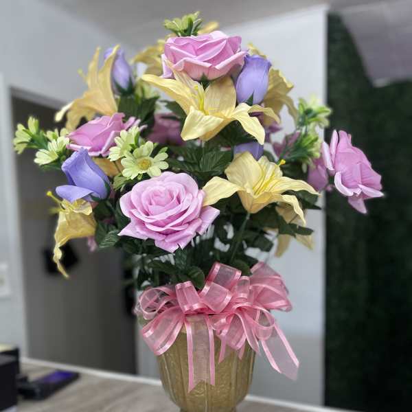 Pink and yellow floral arrangement in a gold vase with a pink ribbon bow