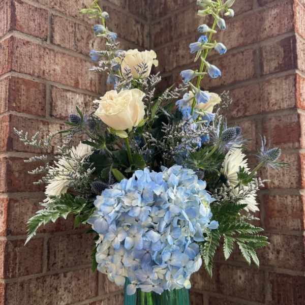 Blue hydrangea and white rose arrangement in a teal glass vase
