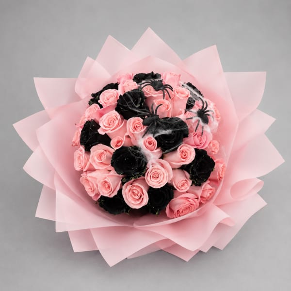 Pink and black rose bouquet wrapped in pale pink paper with spider decorations