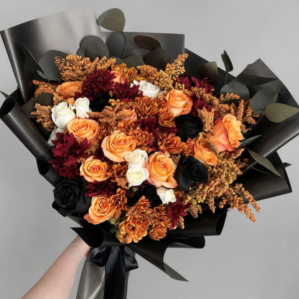 Bouquet of orange, white, and dark red flowers wrapped in black paper
