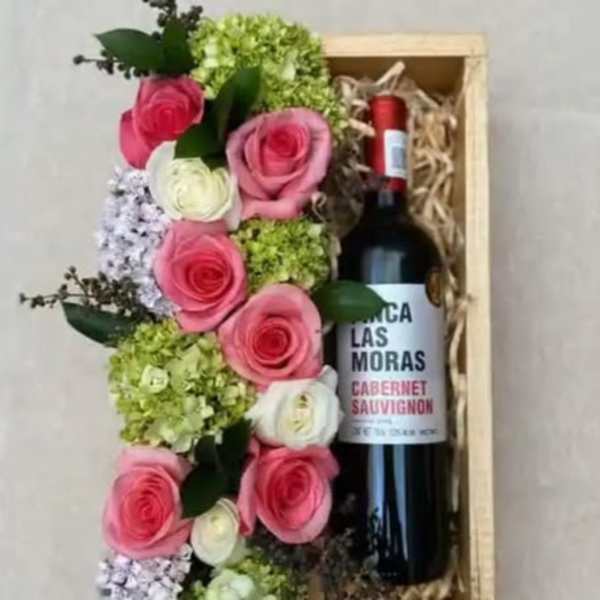 Pink and white roses arranged beside a wine bottle in a wooden gift box