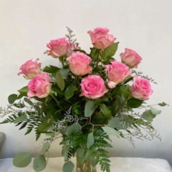 Pink roses arranged in a clear glass vase with greenery